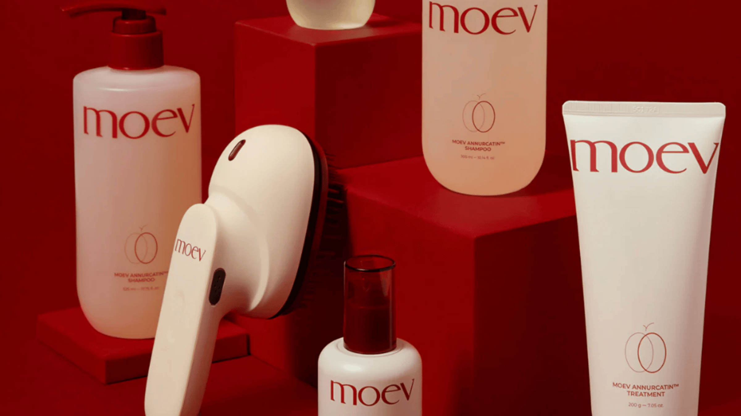 MOEV Annurcatin™ hårvårdsprodukter arrangerade på röd bakgrund. Bilden visar schampo, treatment, hårolja och hårborste från MOEV – en exklusiv koreansk hårvårdsserie med naturliga ingredienser.