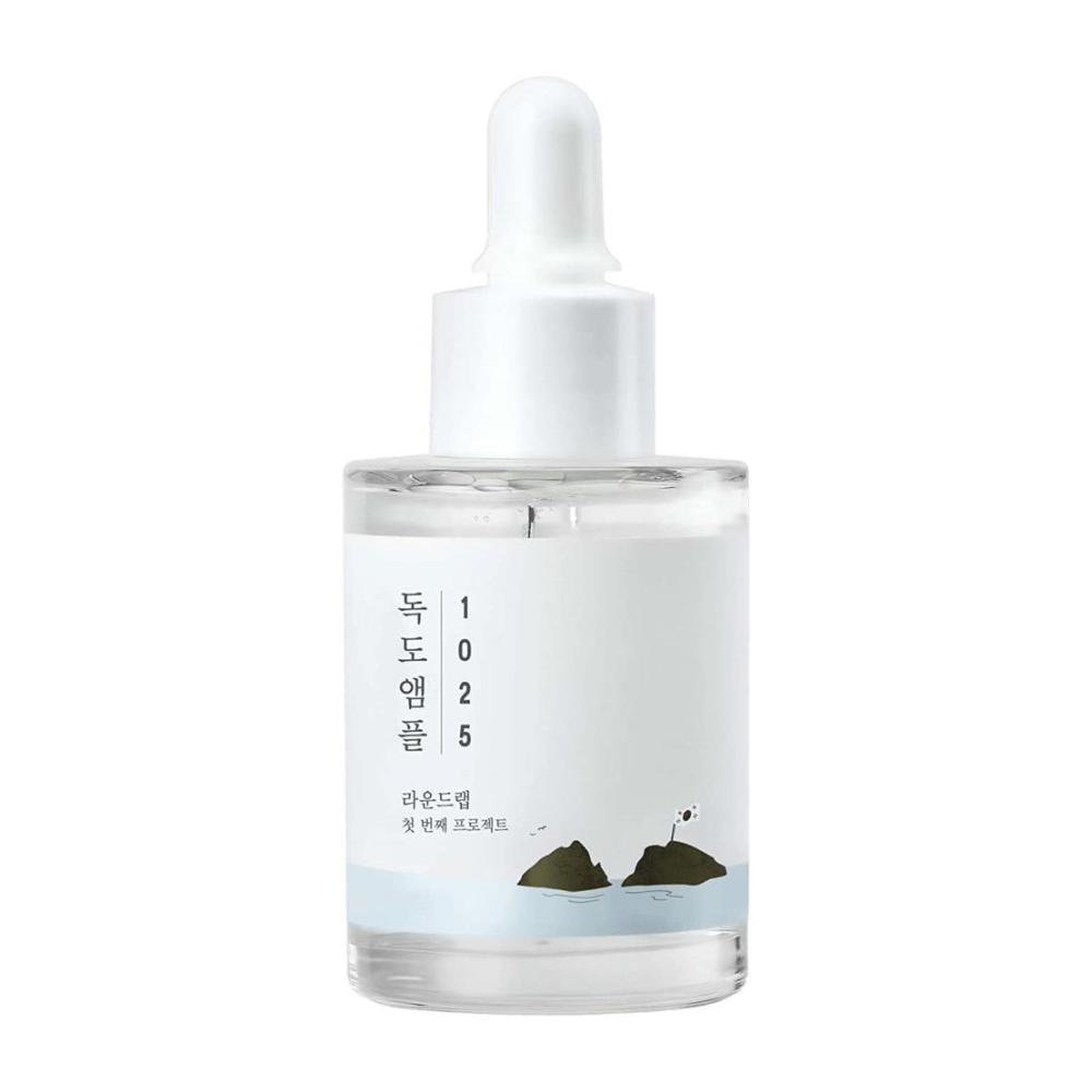 Prozorna steklenička z obraznim serumom 1025 Dokdo Ampoule, okrašena z minimalistično morsko temo, na beli podlagi.
