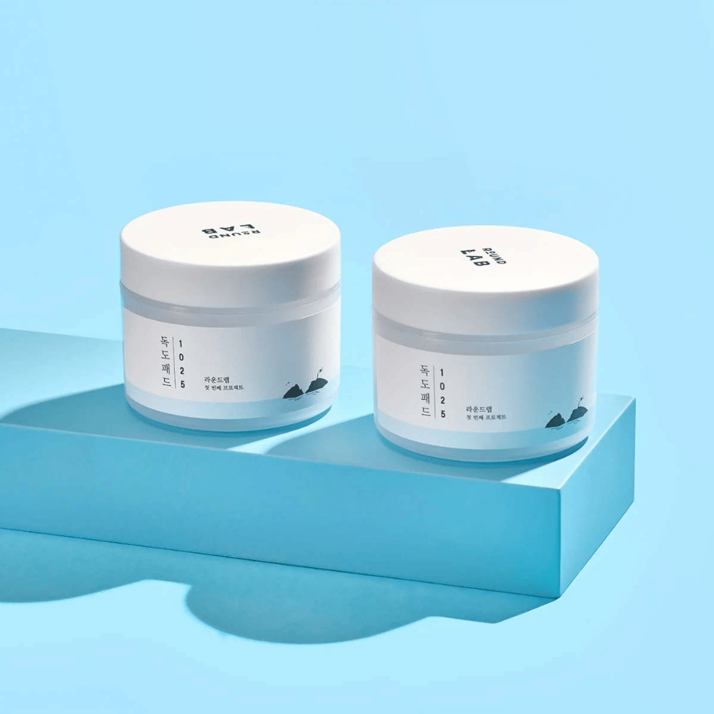 Dva bela kozarca 1025 Dokdo Pads, postavljena na svetlo modro polico, ki meče odsev, na modri podlagi.