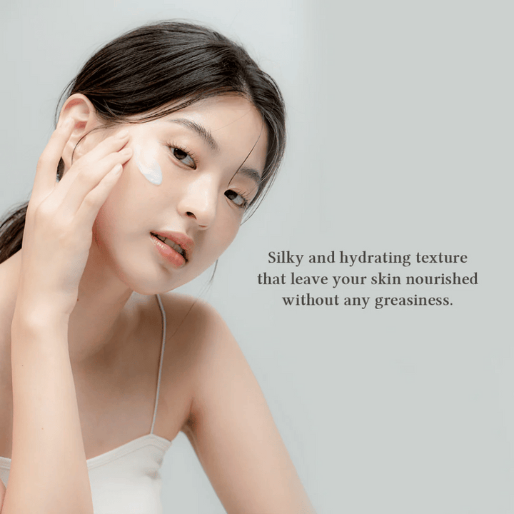 Slika prikazuje žensko, ki nanaša kremo za kožo na svoj obraz. Besedilo na sliki opisuje izdelek kot svilnato in vlažilno ter poudarja, da neguje kožo brez mastnega občutka. To nakazuje, da ima krema lahko in prijetno teksturo, ki se dobro vpije v kožo.