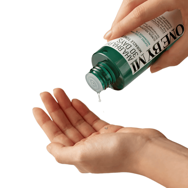 Roka drži zeleno steklenico z napisom "AHA, BHA, PHA 30 Days Miracle Toner" in iztisne prozorno tekočino v dlan druge roke, pripravljena za uporabo.