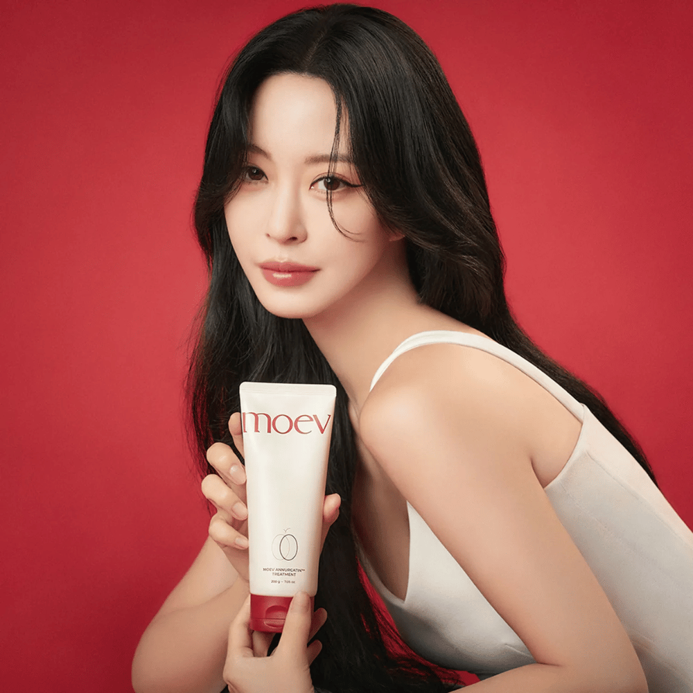 Ženska z dolgimi, sijočimi lasmi drži MOEV Annurcatin Treatment – korejska nega las, ki zagotavlja hranila, moč in sijaj z naravnimi sestavinami.