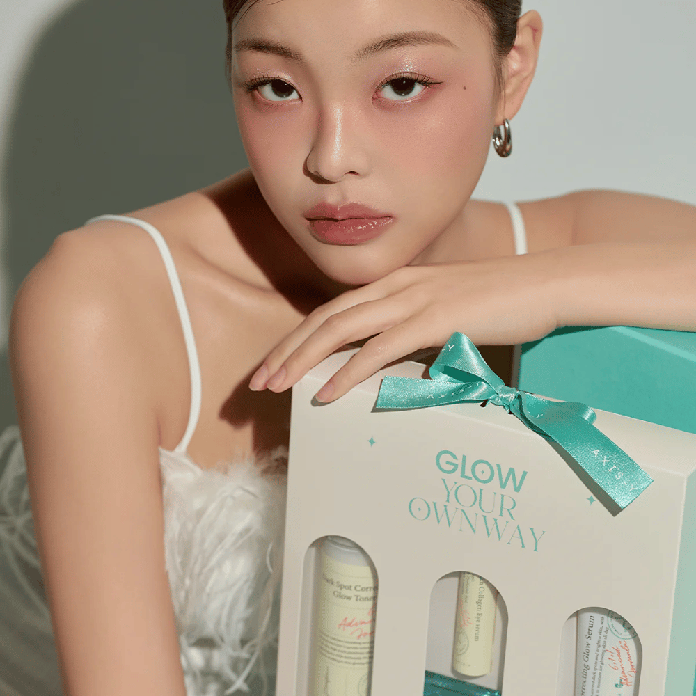 Manekenka z elegantnim ličenjem drži darilno škatlo AXIS-Y 'Glow Your Own Way' – stilski komplet za nego kože, popoln kot darilo zase ali za nekoga, ki ga imate radi.