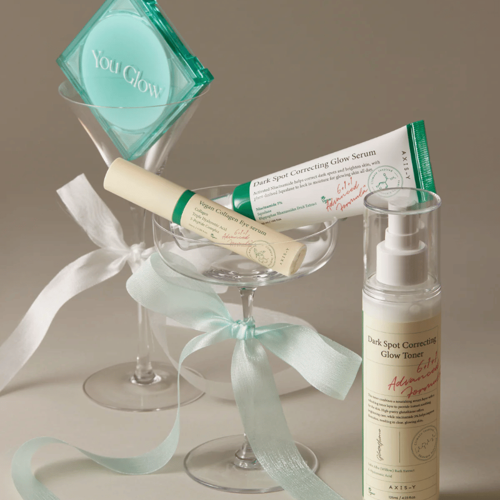 Slika kompleta za nego kože AXIS-Y z očesnim serumom, serumom in tonerjem – elegantno postavljeni v koktajl kozarec s svilenim trakom, popolno za luksuzno predstavitev darila.