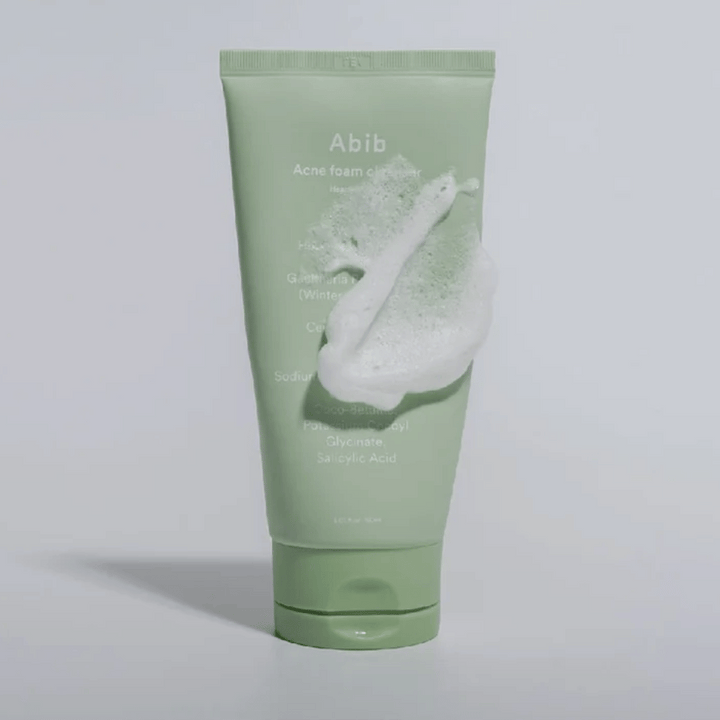 Zelena tuba z Abib Acne Foam Cleanser Heartleaf, pokrita z belo peno, ki ponazarja učinek penjenja čiščenja. Izdelek vsebuje ekstrakt srčastega lista in salicilno kislino za kožo, nagnjeno k aknam.
