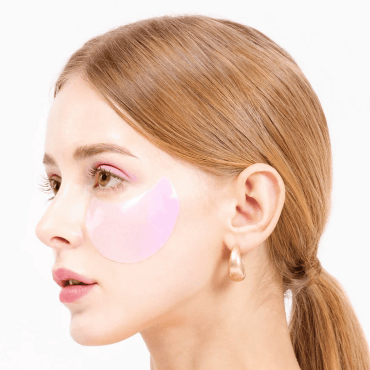 Model nosi rožnat hidrogelni obliž za oči pod očesom, vlaži in pomlajuje kožo.