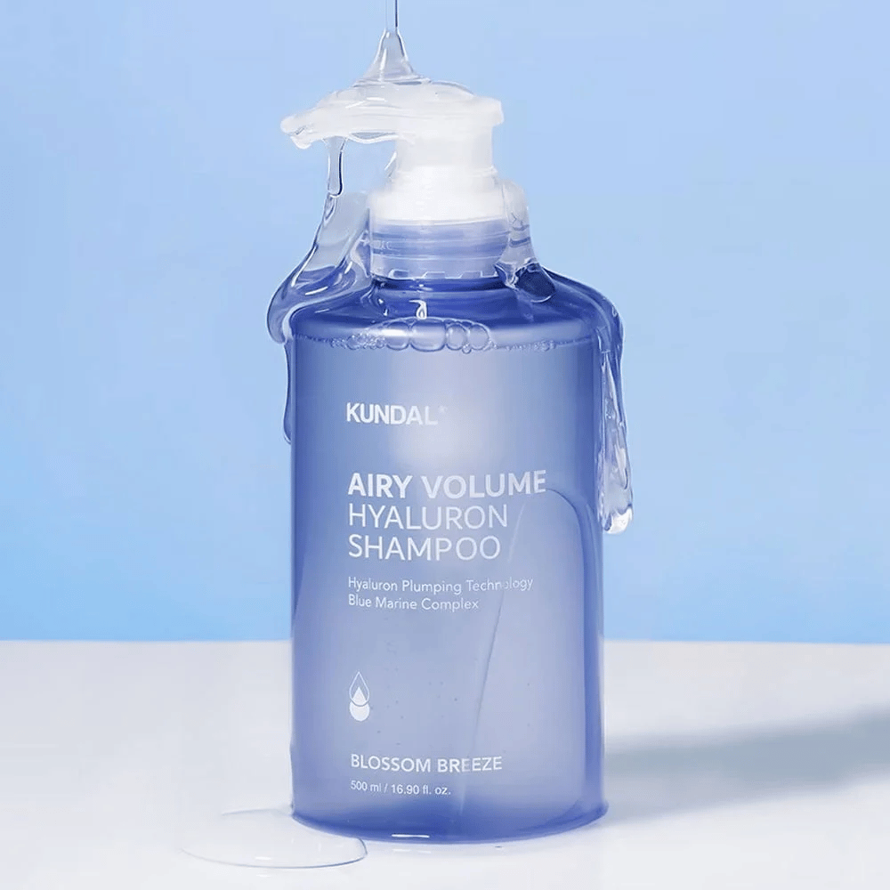 KUNDAL Airy Volume Hyaluron Shampoo Blossom Breeze v modri steklenički s črpalko, s hialuronom in Blue Marine Complex, fotografirano s tekočo vodo.