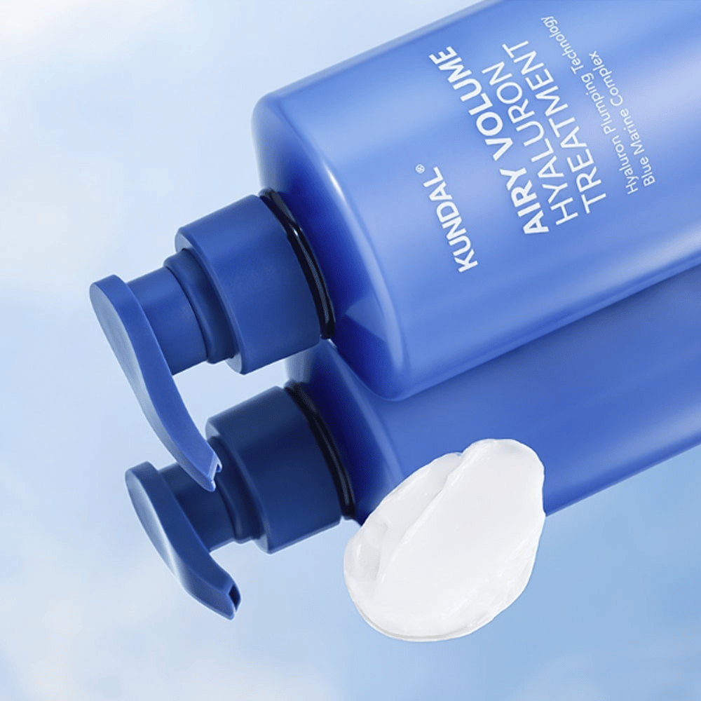 KUNDAL Airy Volume Hyaluron Treatment v modri steklenički s črpalko ležeče, z vidnim belim kremnim izdelkom poleg.