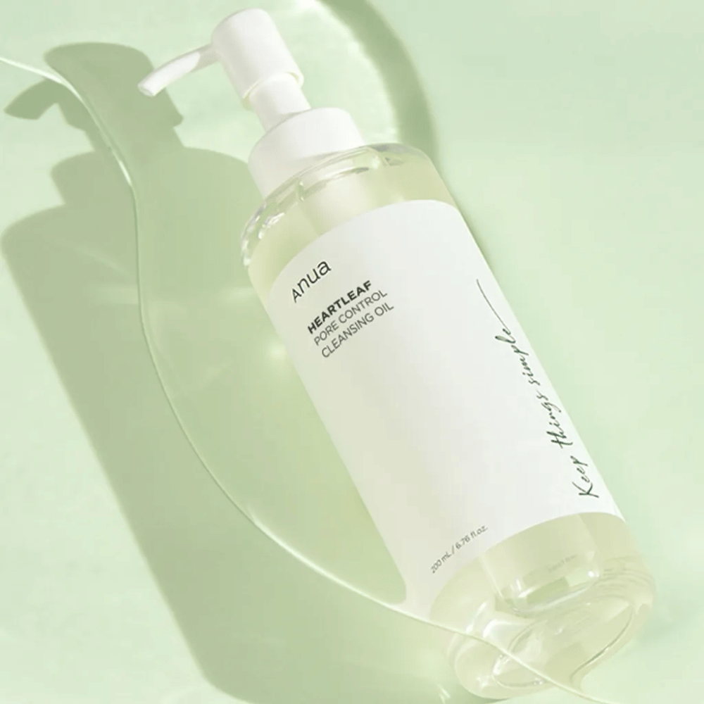 Na sliki je ANUA Heartleaf Pore Control Cleansing Oil, čistilno olje z dizajnom črpalke. Steklenica je prozorna, vsebina pa izgleda kot lahka, oljna konsistenca. Etiketa nosi logotip blagovne znamke in ime izdelka v preprostem in elegantnem besedilu, kar prispeva k občutku minimalistične lepote in čistosti. Del dizajna je napis "Keep things simple", kar nakazuje na filozofijo enostavnosti v rutini nege kože. Steklenica vsebuje 200 ml izdelka.