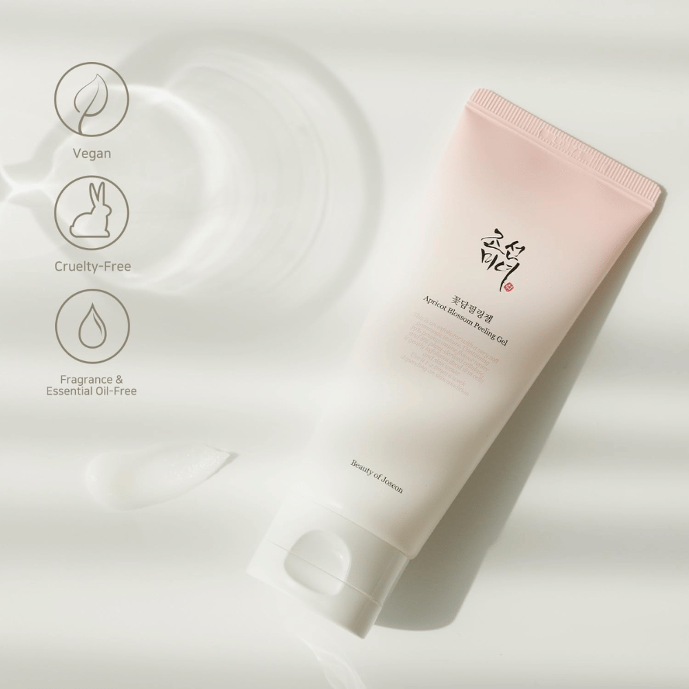 Tuba z Apricot Blossom Peeling Gel leži na odsevni površini z ikonami, ki označujejo, da je izdelek veganski, prijazen do živali in brez vonja ter eteričnih olj.