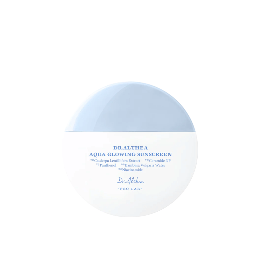 Slika izdelka Dr. Althea Aqua Glowing Sunscreen – okrogla krema za sončenje v beli in svetlo modri embalaži z modrim besedilom, ki poudarja vlažilne sestavine, kot sta niacinamid in ceramidi.