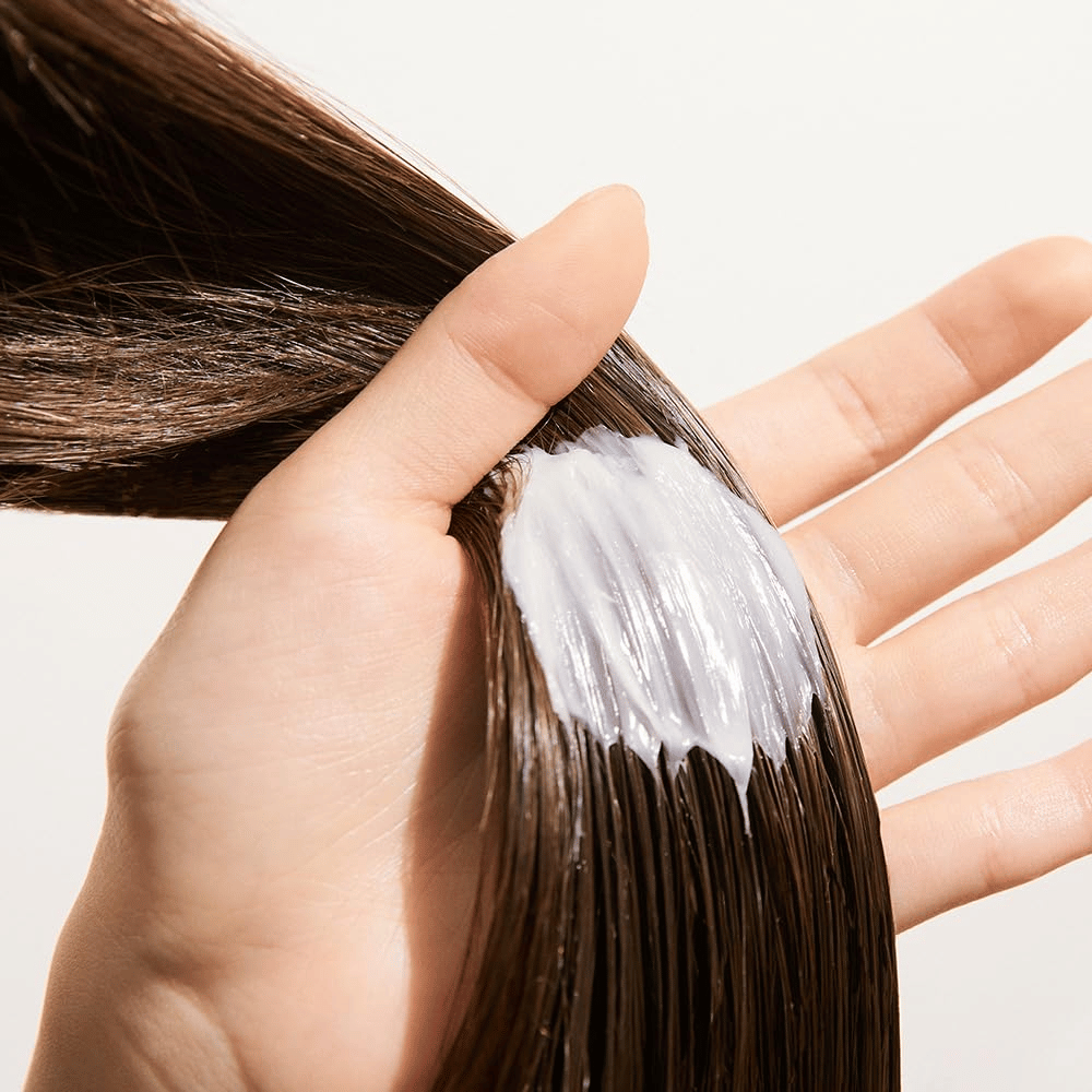 Roka nanaša Nature Republic Argan Essential Moisture Repairing Hair Mask na mokre lase – vlažilna maska, ki krepi in mehča lase.