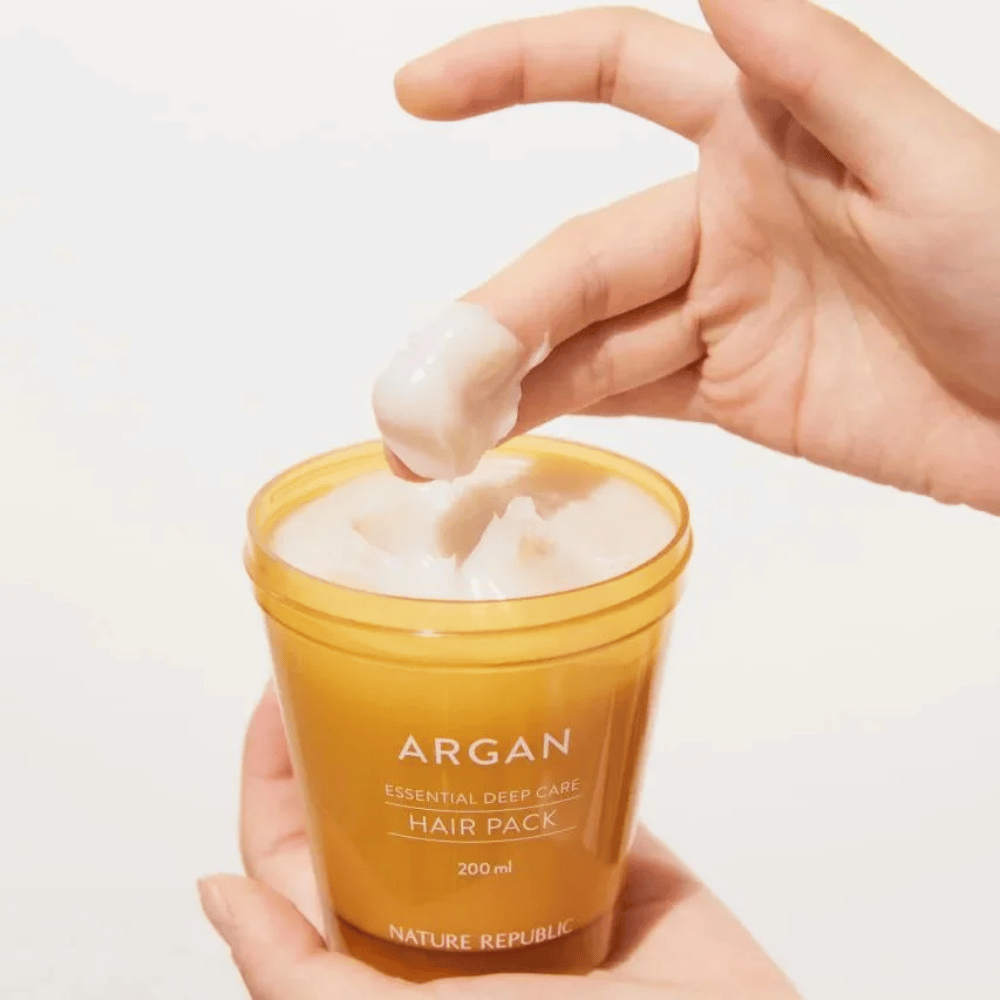 Roka vzame kremasto formulo iz Nature Republic Argan Essential Moisture Repairing Hair Mask – intenzivna nega za suhe lase.