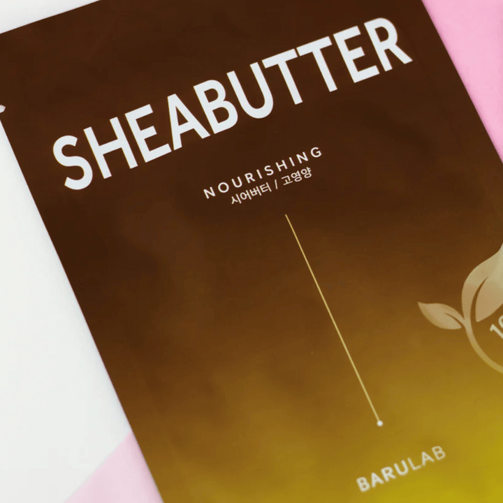 Bližnji posnetek embalaže maske BARULAB "SHEABUTTER Nourishing". Izdelek je označen kot "100% Vegan Product" in ima barvni prehod iz temno rjave v svetlo rjavo.