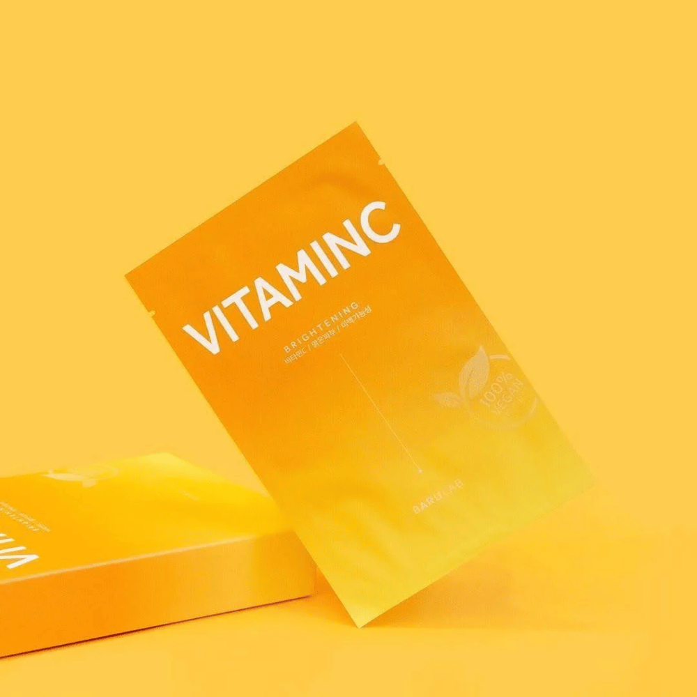 Kup pakiranj mask BARULAB "VITAMINC Brightening", vse označene kot "100% Vegan Product". Pakiranja imajo barvni ton v različnih odtenkih oranžne in rumene, postavljena na enotno rumeno ozadje.