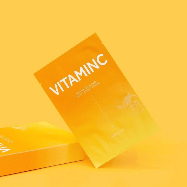 Kup pakiranj mask BARULAB "VITAMINC Brightening", vse označene kot "100% Vegan Product". Pakiranja imajo barvni ton v različnih odtenkih oranžne in rumene, postavljena na enotno rumeno ozadje.