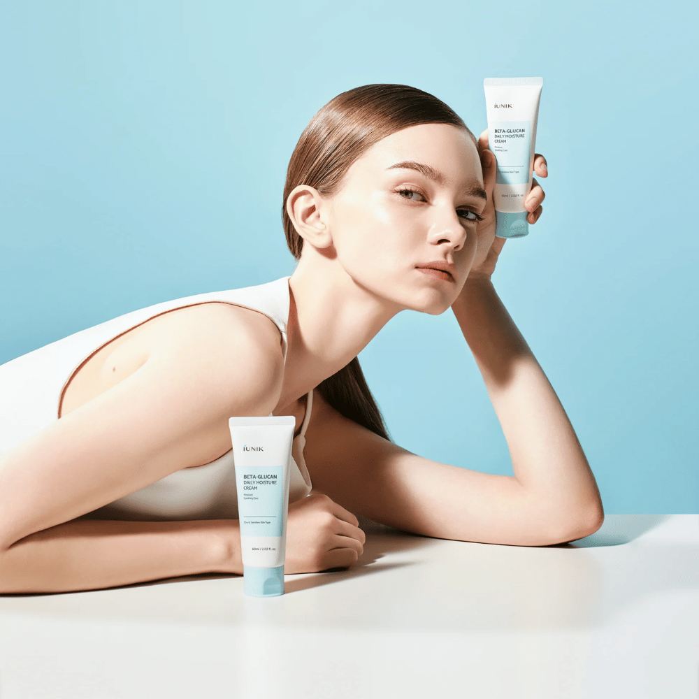 Življenjska slika, na kateri model pozira z iUNIK Beta-Glucan Daily Moisture Cream na svetlo modrem ozadju. Slika posreduje čist, svež in vlažilen občutek, hkrati pa je izdelek jasno izpostavljen.