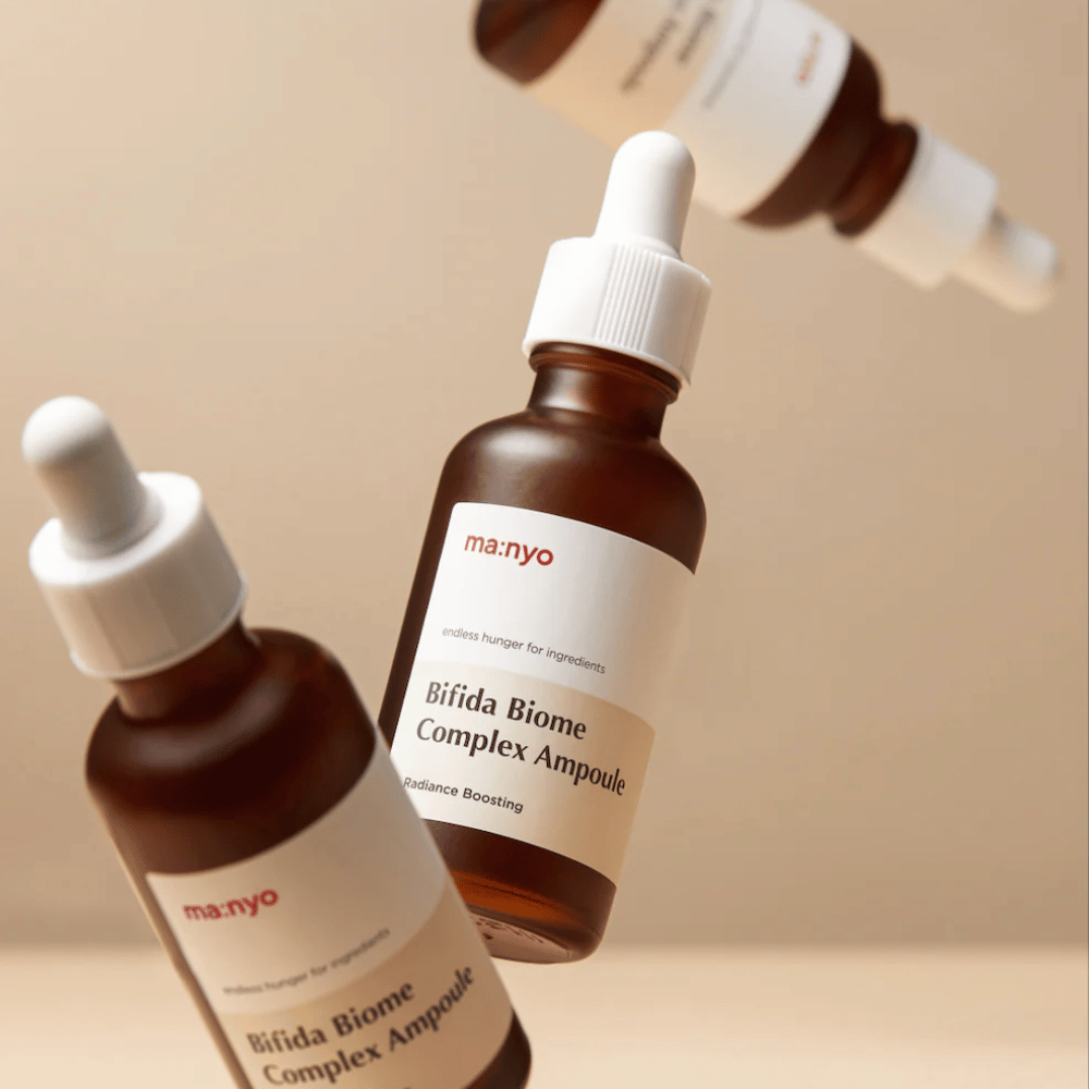 Slika izdelka z več lebdečimi stekleničkami ma:nyo Bifida Biome Complex Ampoule na bež ozadju, ki daje moderen in minimalističen občutek.