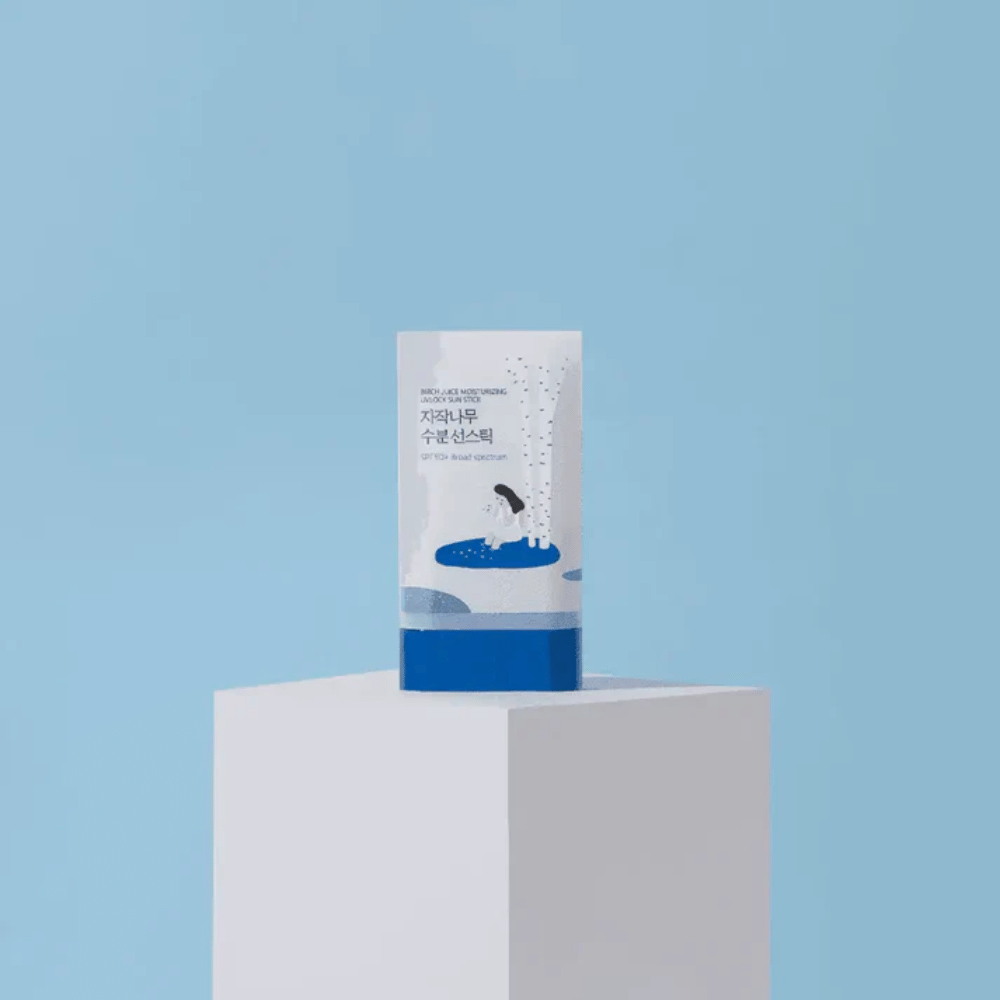 ROUND LAB Birch Juice Moisturizing Sun Stick SPF50+ stoji na podstavku pred modrim ozadjem – vlažilna zaščita pred soncem v stiku