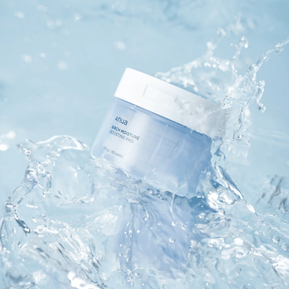 Slika Anuas "Birch Moisture Boosting Pad" v prozorni modri posodi s kapljicami vode okoli, kar nakazuje na vlažilni učinek izdelka.