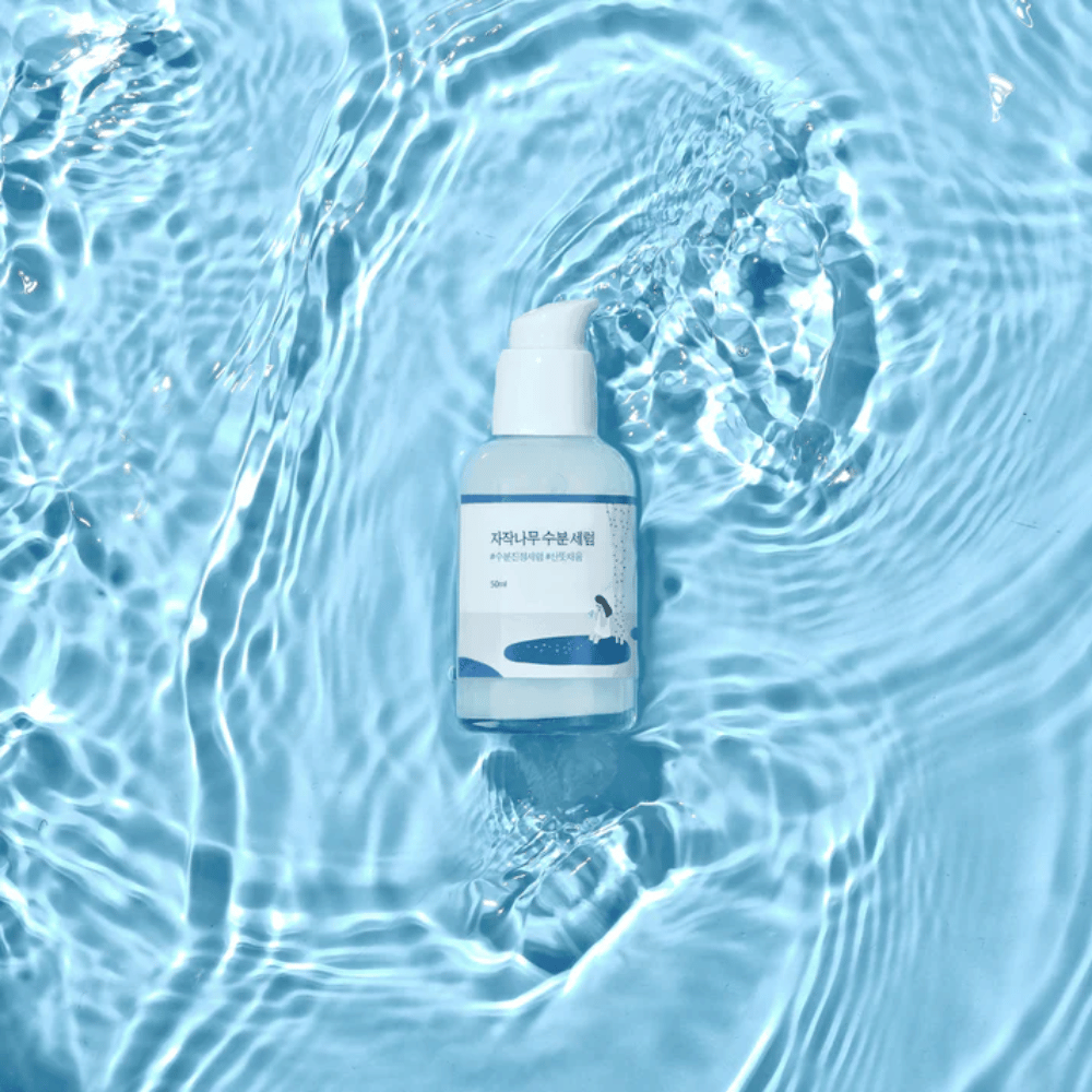 Round Lab Birch Juice Moisturizing Serum v steklenički s črpalko, ki plava na modri vodi z odsevi sončne svetlobe.