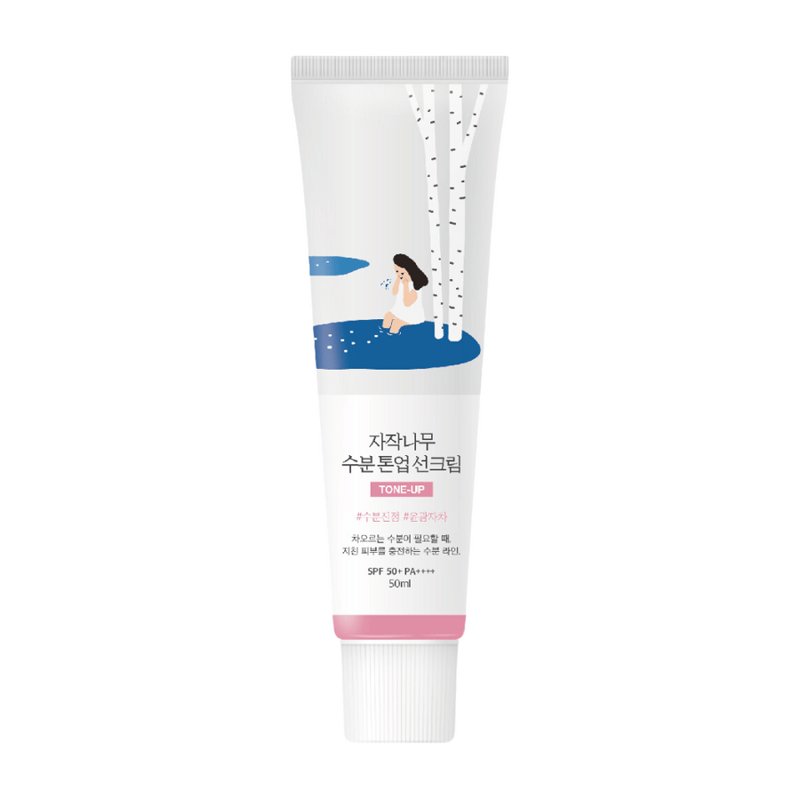 Bela tuba z Birch Juice Moisturizing Tone Up Sunscreen. Tuba ima ilustracijo ženske, ki sedi ob brezi poleg luže. Besedilo na tubi je v korejščini in navaja, da ima izdelek SPF 50+ PA++++ in vsebuje 50 ml.