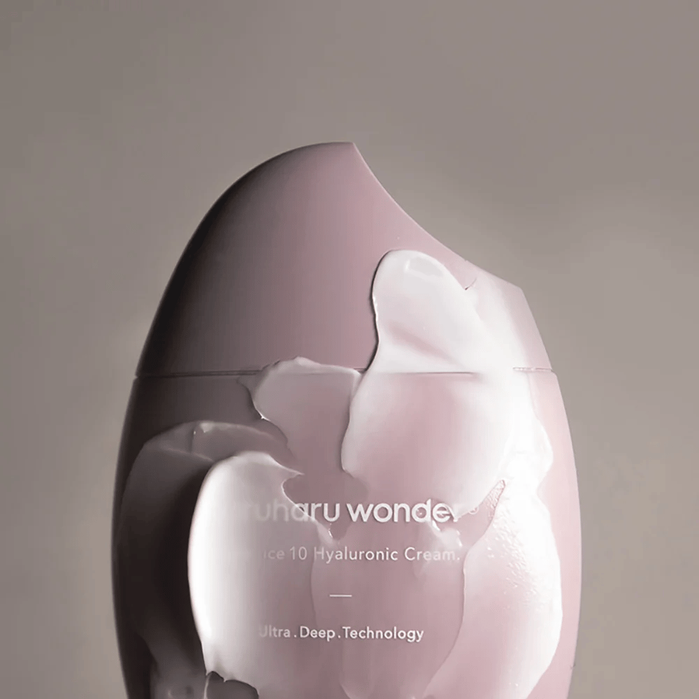 Slika prikazuje kozarec "Haruharu Wonder Black Rice 10 Hyaluronic Cream", ki je delno prekrit z gosto, prozorno kremo. Besedilo na sliki nakazuje uporabo napredne tehnologije za globinsko vlaženje kože. Oblikovanje je moderno in minimalistično.