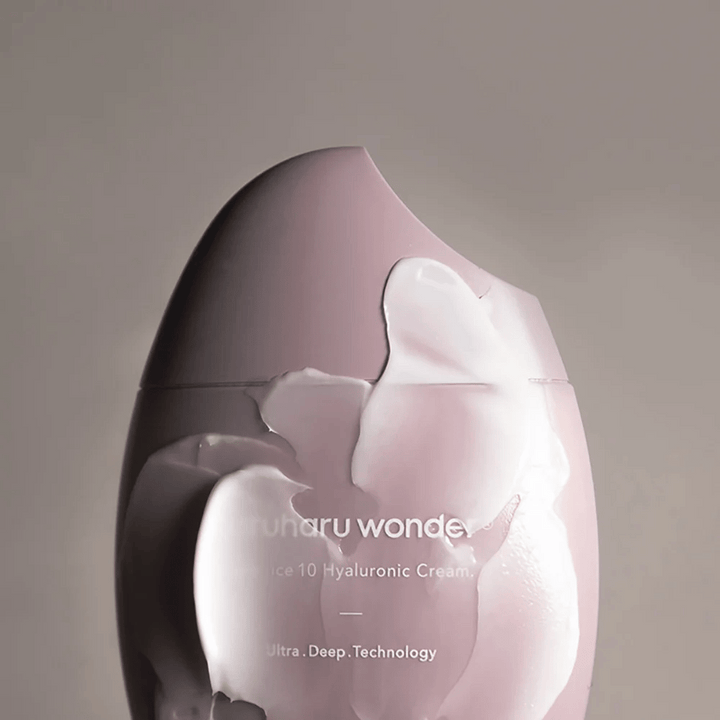 Slika prikazuje kozarec "Haruharu Wonder Black Rice 10 Hyaluronic Cream", ki je delno prekrit z gosto, prozorno kremo. Besedilo na sliki nakazuje uporabo napredne tehnologije za globinsko vlaženje kože. Oblikovanje je moderno in minimalistično.