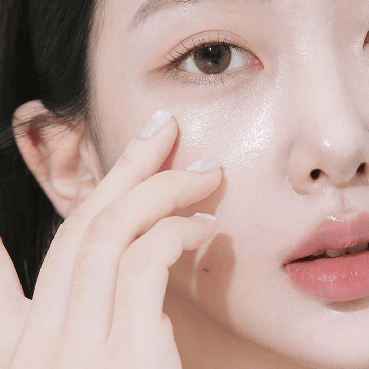 Povečava ženske, ki s konicami prstov nanaša kremo za oči pod očesom. Koža je videti navlažena, sijoča in negovana z naravnim sijajem.