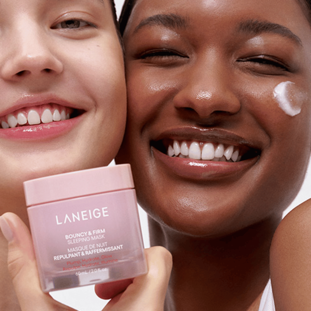 Dve osebi se smejita in držita Laneige Bouncy & Firm Sleeping Mask. Ena izmed njiju je nanesla masko na svoj obraz, izdelek pa je jasno viden v njihovih rokah. Maska je v roza lončku in se trži kot "Polnjenje, Vlaženje, Sijaj."