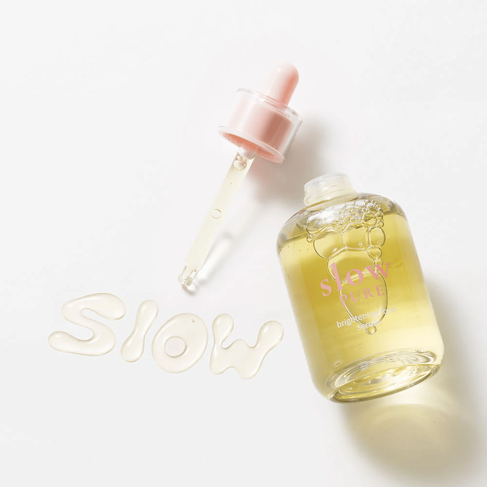 Slow Pure Brightening Tone Serum z odprto pipeto, besedilo napisano v serumu na površini: "Slow".