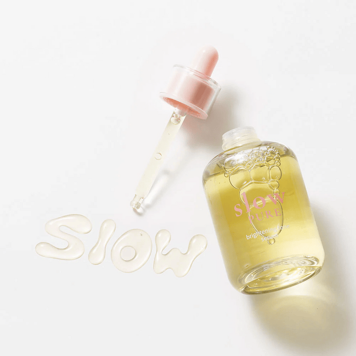 Slow Pure Brightening Tone Serum z odprto pipeto, besedilo napisano v serumu na površini: "Slow".