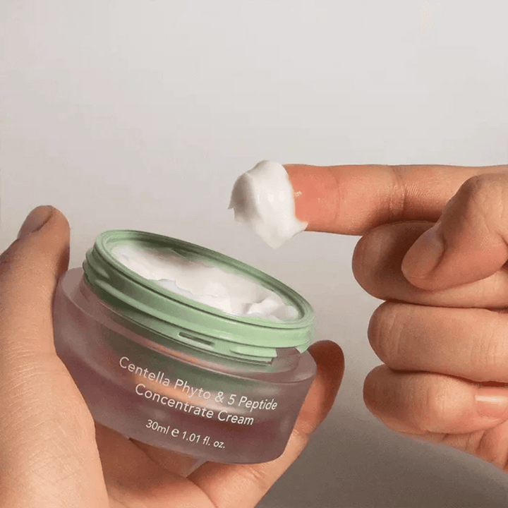 Roka, ki vzame klik Centella Phyto & 5 Peptide Concentrate Cream iz posode.