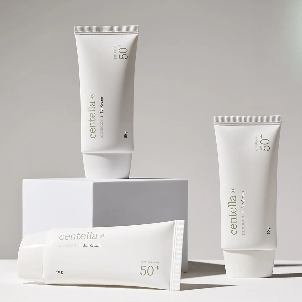 Tri embalaže Centella Sun Cream SPF 50+ PA++++ estetsko urejene na belih podstavkih. Dve tubi stojita pokonci, ena pa leži, vse z belo, minimalistično zasnovo in zelenimi tekstualnimi podrobnostmi.