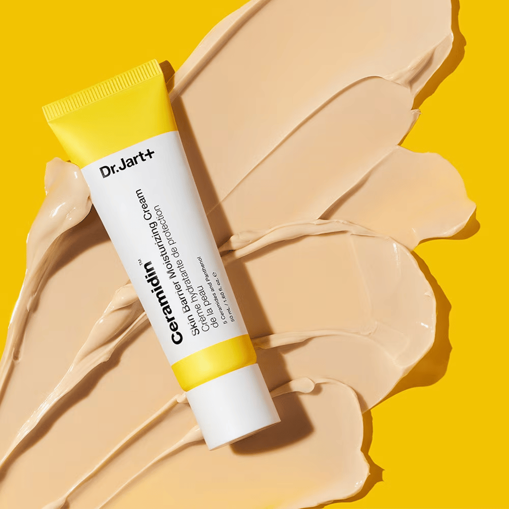 Tuba z Dr. Jart+ Ceramidin Skin Barrier Moisturizing Cream na rumeni podlagi z razpršeno kremo.