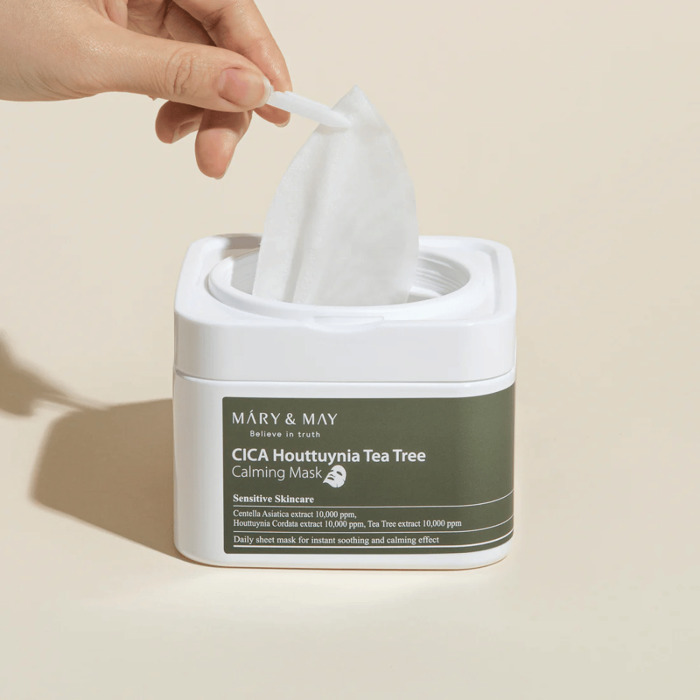Roka, ki dviguje masko iz lončka Mary & May Cica Houttuynia Tea Tree Calming Mask – pomirjujoča obrazna maska za občutljivo kožo s Cica in izvlečkom čajevca.