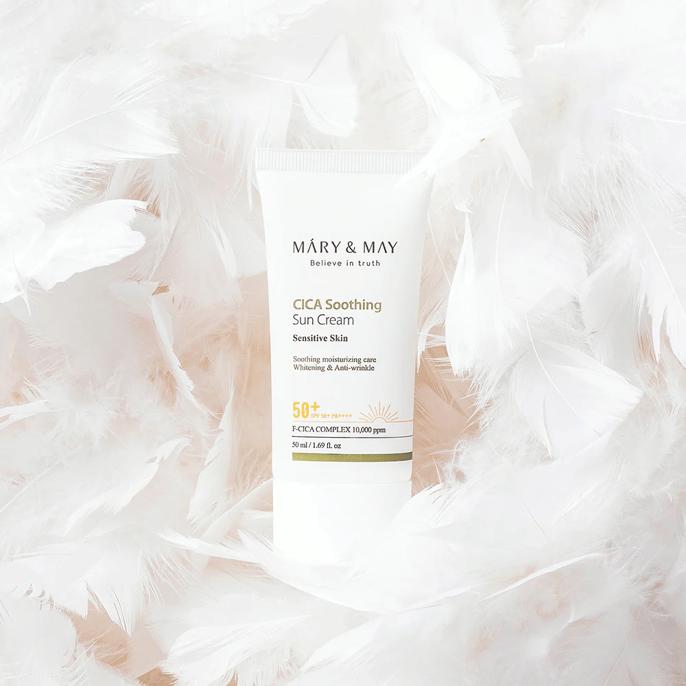 Mary&May CICA Soothing Sun Cream obdan z mehkimi belimi peresi. Slika izraža občutek nežnosti, udobja in lahke formule, prilagojene občutljivi koži.