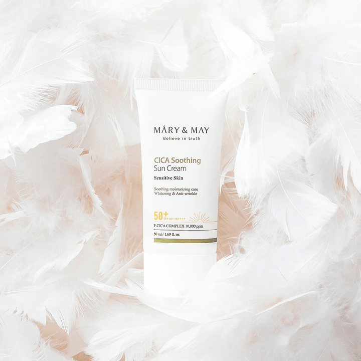 Mary&May CICA Soothing Sun Cream obdan z mehkimi belimi peresi. Slika izraža občutek nežnosti, udobja in lahke formule, prilagojene občutljivi koži.