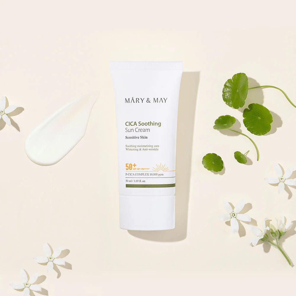 Mary&May CICA Soothing Sun Cream SPF50+ PA++++ predstavljen skupaj s kremasto teksturo, listi centelle in belimi cvetovi. Slika izpostavlja pomirjujoče lastnosti izdelka in osredotočenost na občutljivo kožo.