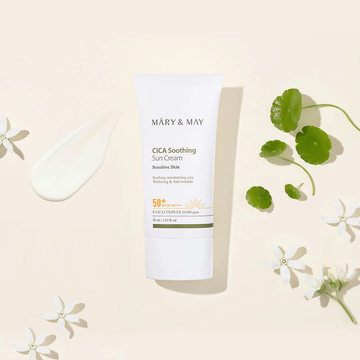 Mary&May CICA Soothing Sun Cream SPF50+ PA++++ predstavljen skupaj s kremasto teksturo, listi centelle in belimi cvetovi. Slika izpostavlja pomirjujoče lastnosti izdelka in osredotočenost na občutljivo kožo.