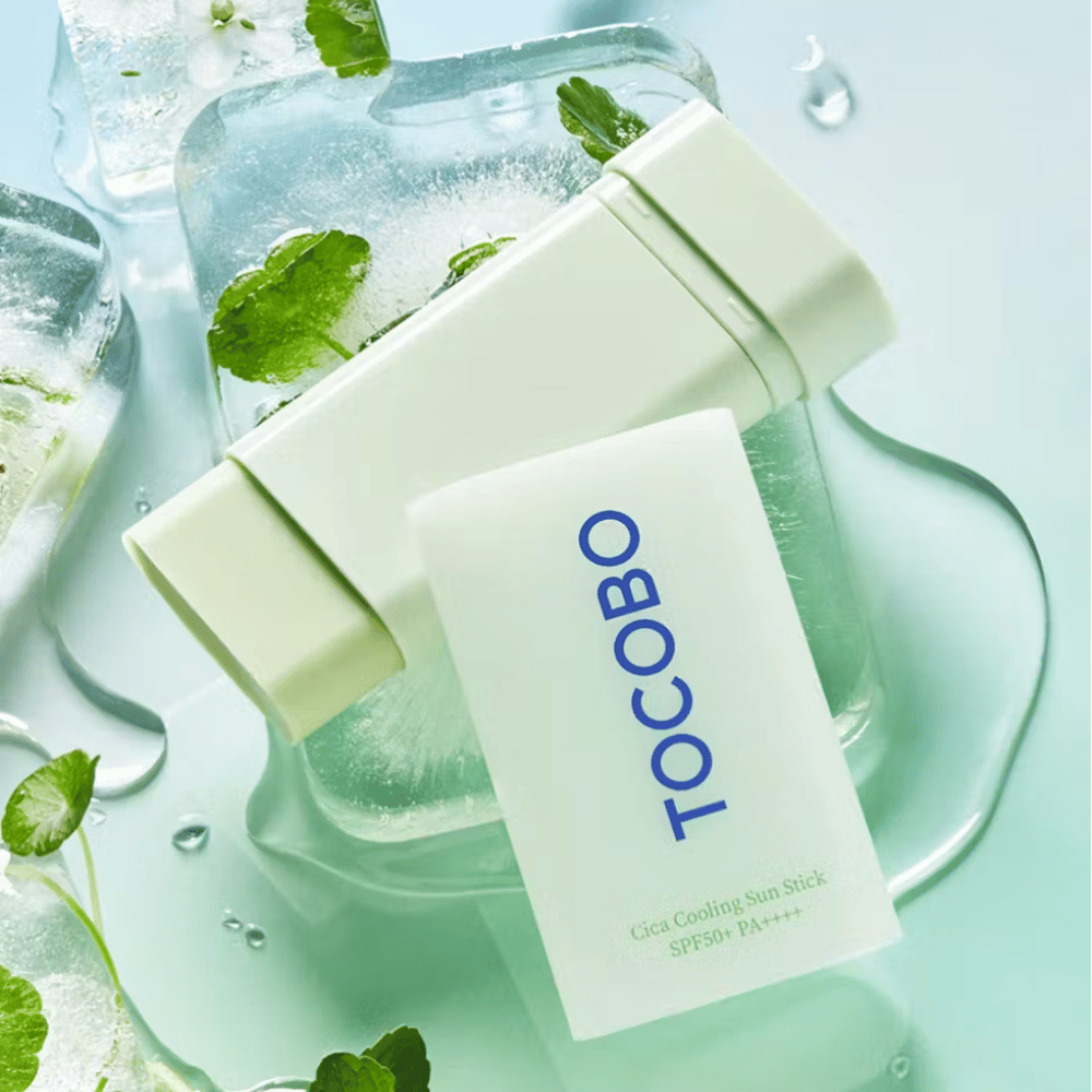 Tocobo Cica Cooling Sun Stick SPF50+ PA++++ na ledenih kockah z zelenimi rastlinskimi listi, kar prenaša hladen in osvežujoč občutek.