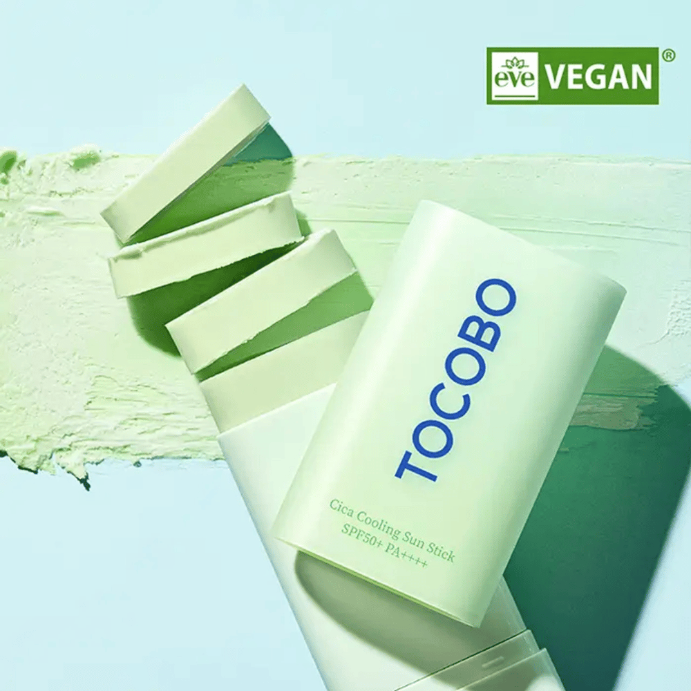 Tocobo Cica Cooling Sun Stick SPF50+ PA++++ v svetlo zeleni embalaži z veganskim znakom (EVE VEGAN), ležeča na plasti zelenega sončnega stika.