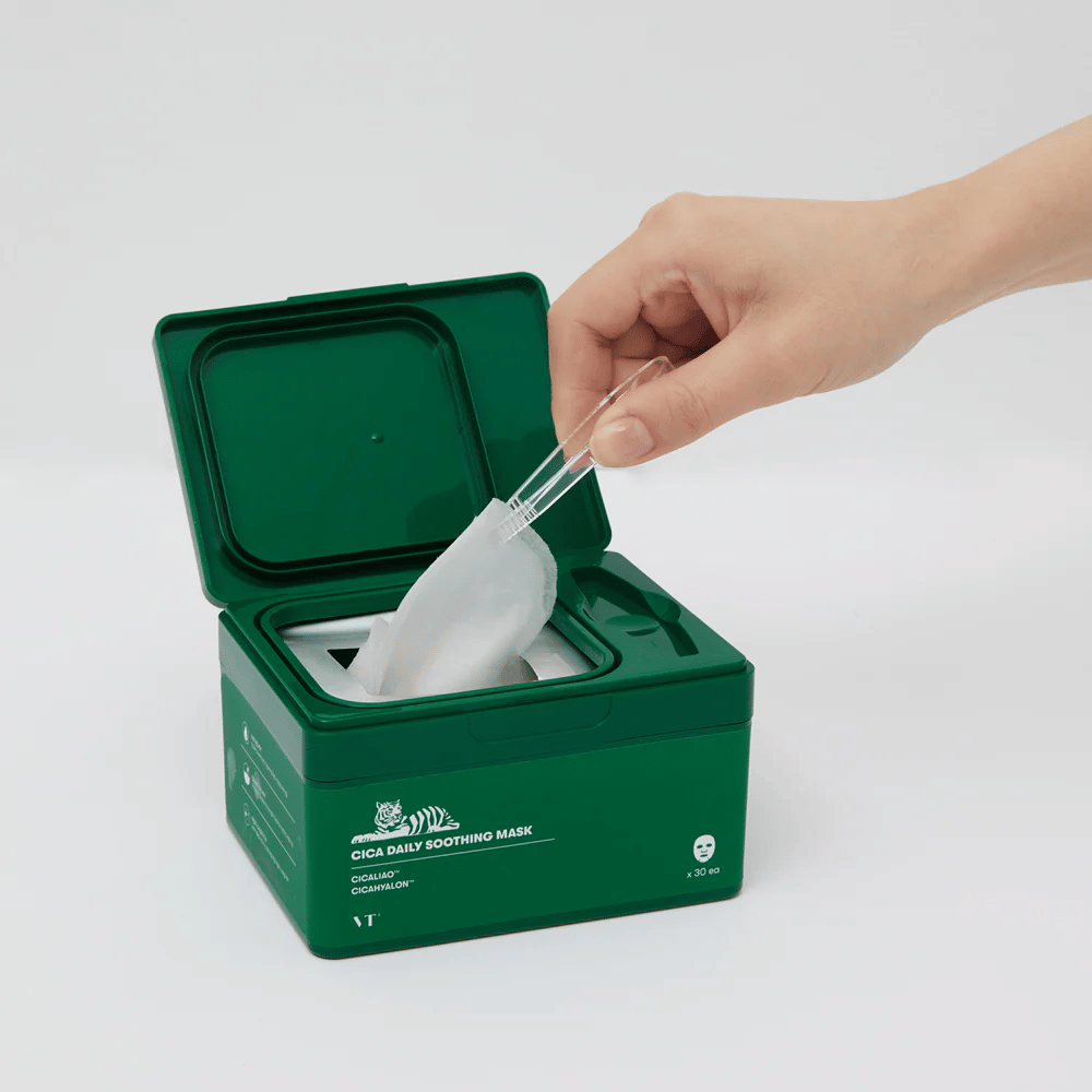 Roka uporablja pinceto za dvig maske iz zelene posode z oznako "Cica Daily Soothing Mask".