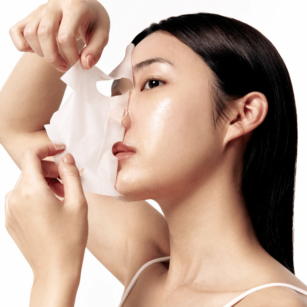 Ženska z gladko, navlaženo kožo odstranjuje belo masko iz listov z obraza, kar razkriva sijočo in enakomerno polt.