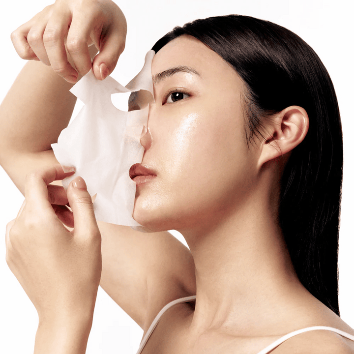 Ženska z gladko, navlaženo kožo odstranjuje belo masko iz listov z obraza, kar razkriva sijočo in enakomerno polt.