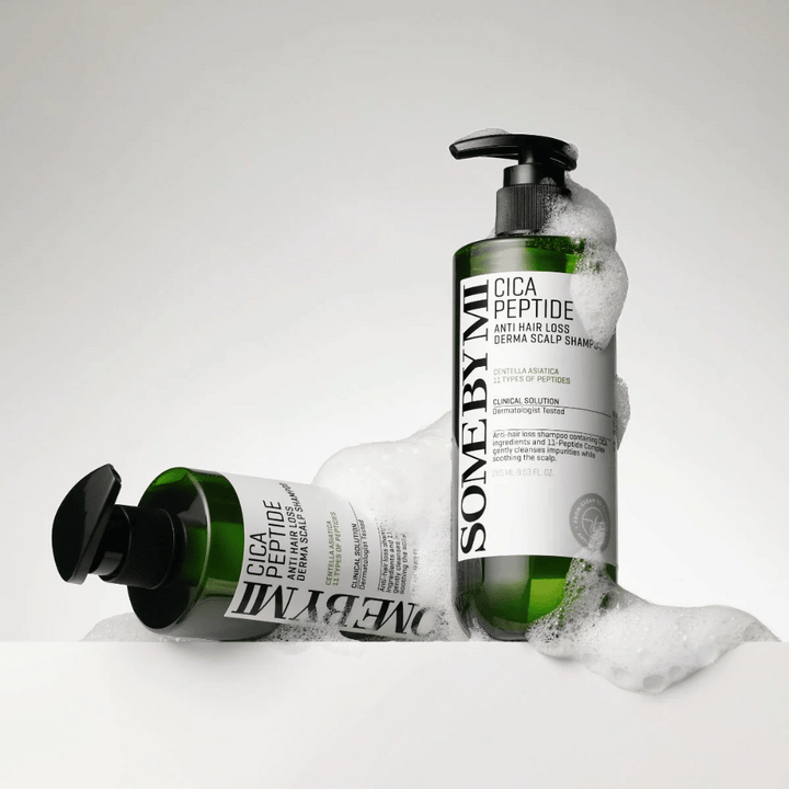 Dve steklenici SOME BY MI Cica Peptide Anti Hair Loss Derma Scalp Shampoo, prekriti s peno, stoje in ležijo na beli podlagi.