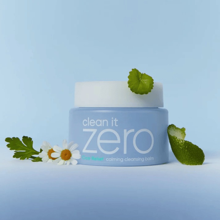 Clean It Zero Cica-Relief Calming Cleansing Balm postavljen z rastlinami in cvetjem, prikazuje nežno čiščenje s pomirjujočo CICA za občutljivo in razdraženo kožo.