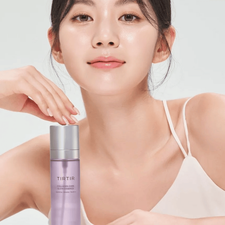 Ženska s sijočo kožo pozira z TIRTIR Collagen Core Glow Essence – sijoča esenca za bolj čvrsto in navlaženo kožo.