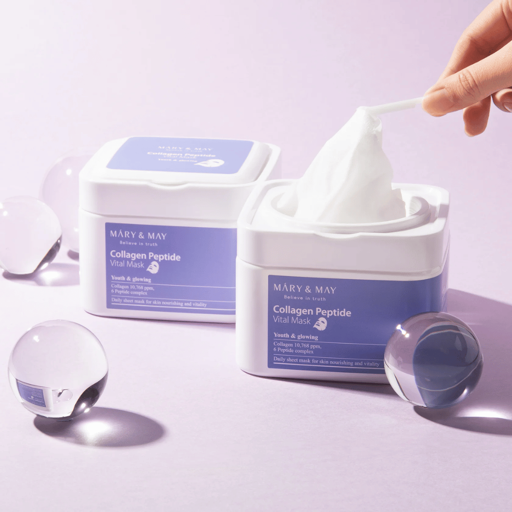 Roka vzame masko iz posode z MARY & MAY Collagen Peptide Vital Mask. Maska je namenjena za vsakodnevno uporabo za hranjenje in sijaj kože, s kolagenom in peptidi za podporo mladostnosti kože.