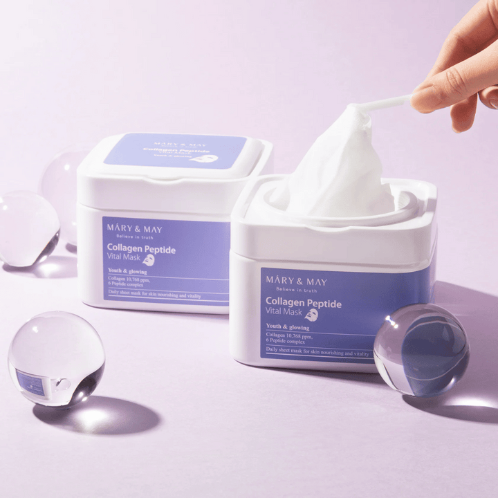 Roka vzame masko iz posode z MARY & MAY Collagen Peptide Vital Mask. Maska je namenjena za vsakodnevno uporabo za hranjenje in sijaj kože, s kolagenom in peptidi za podporo mladostnosti kože.
